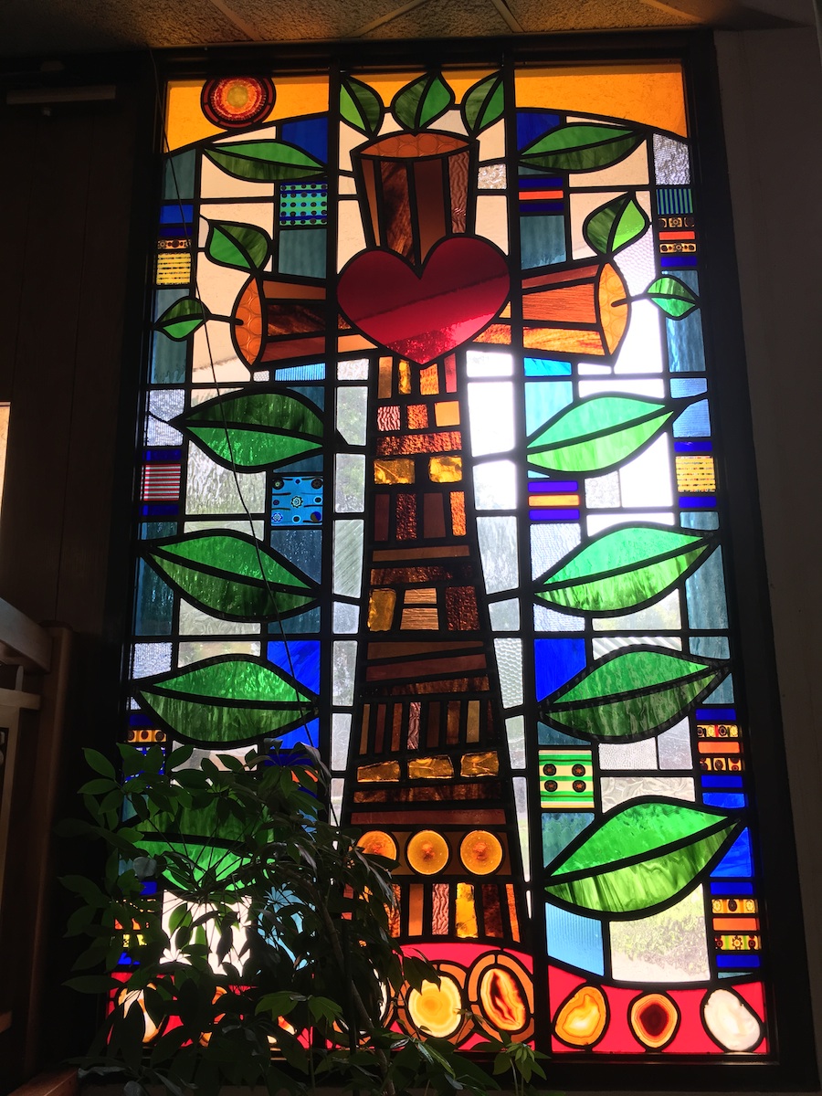 Stained glass window of crucifix features Living Cross with wooden beams and heart at center.